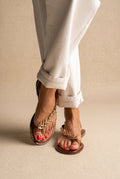 Tan leather flat sandals with gold leaf-shaped toe strap and studded sole edge, front view worn on a model