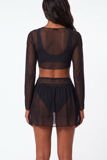 Model wearing black sheer long-sleeve crop top and mesh mini skirt over black bikini, back view