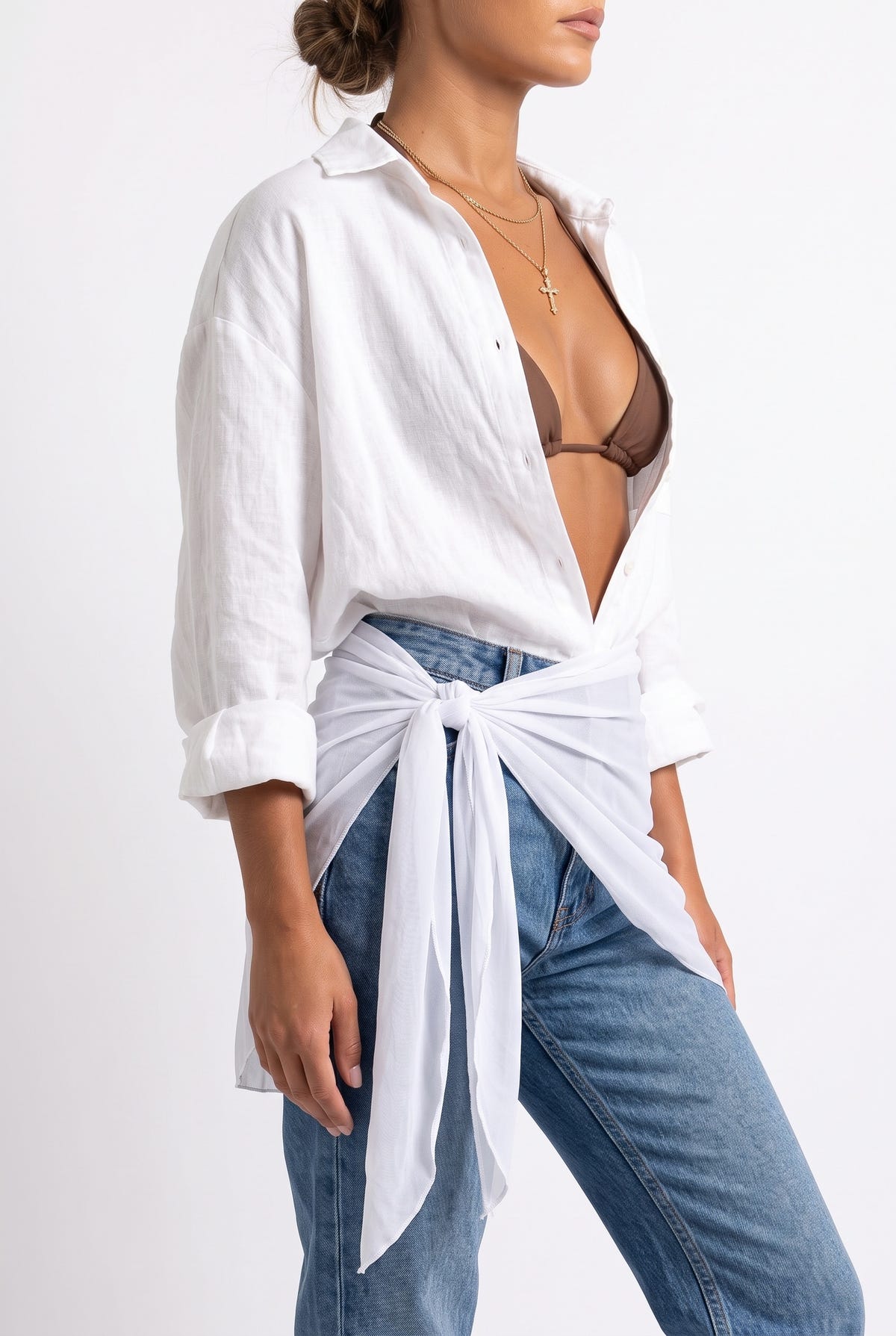 Model wearing white sheer mini pareo tied over open white linen shirt, brown bikini top and blue jeans