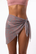 Model wearing terracotta print sheer mini pareo tied at the hip with pink bikini top, front view