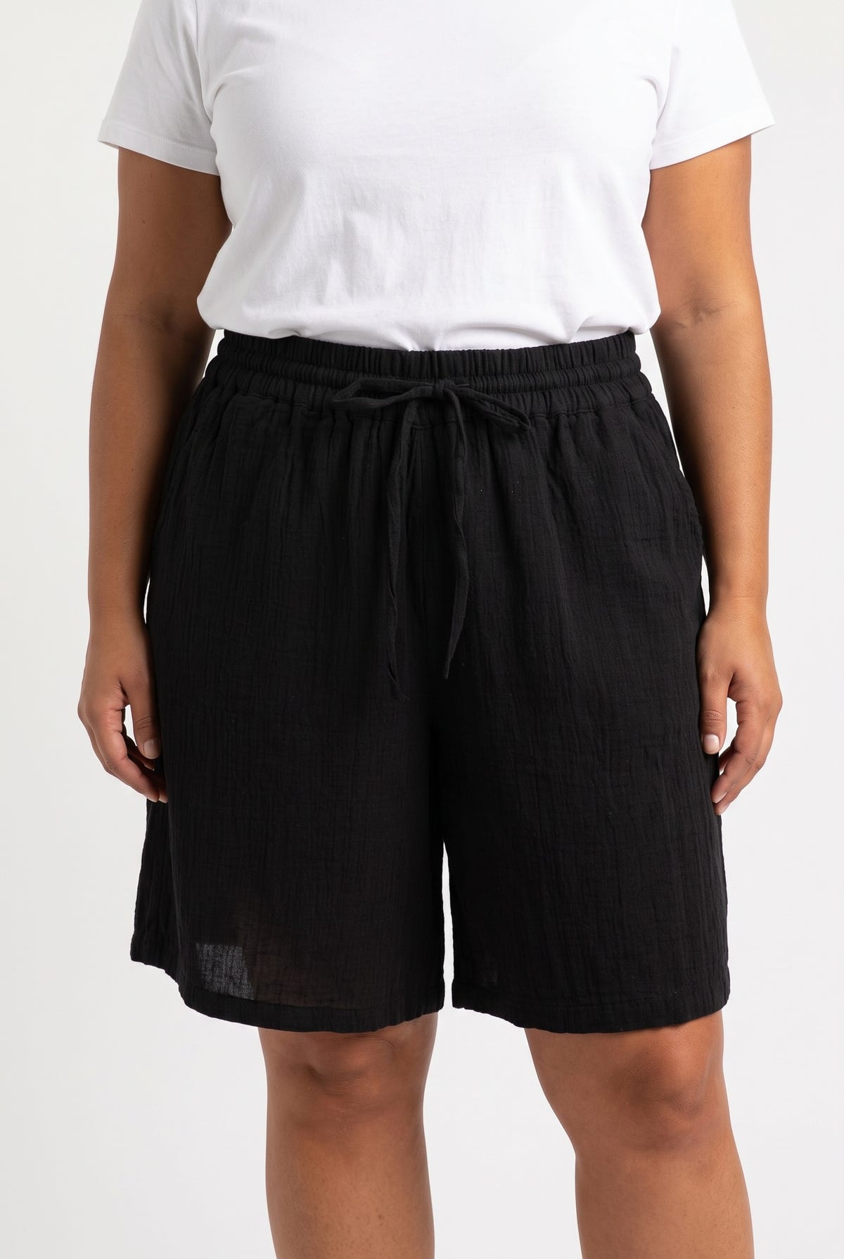 Front view of model wearing black high waisted cotton bermuda shorts with drawstring waist and white t-shirt