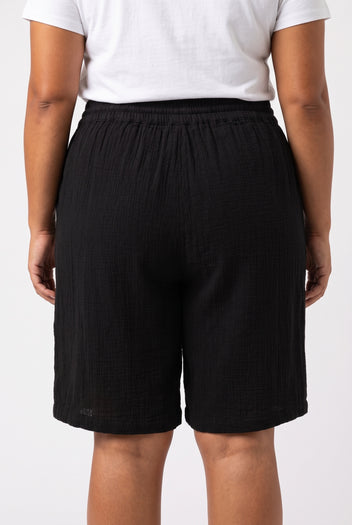 Rear view of model wearing black high waisted cotton bermuda shorts with drawstring waistband and white t-shirt