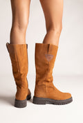 Model legs in tan suede knee-high boots with pull tabs and chunky dark lug soles, rear view