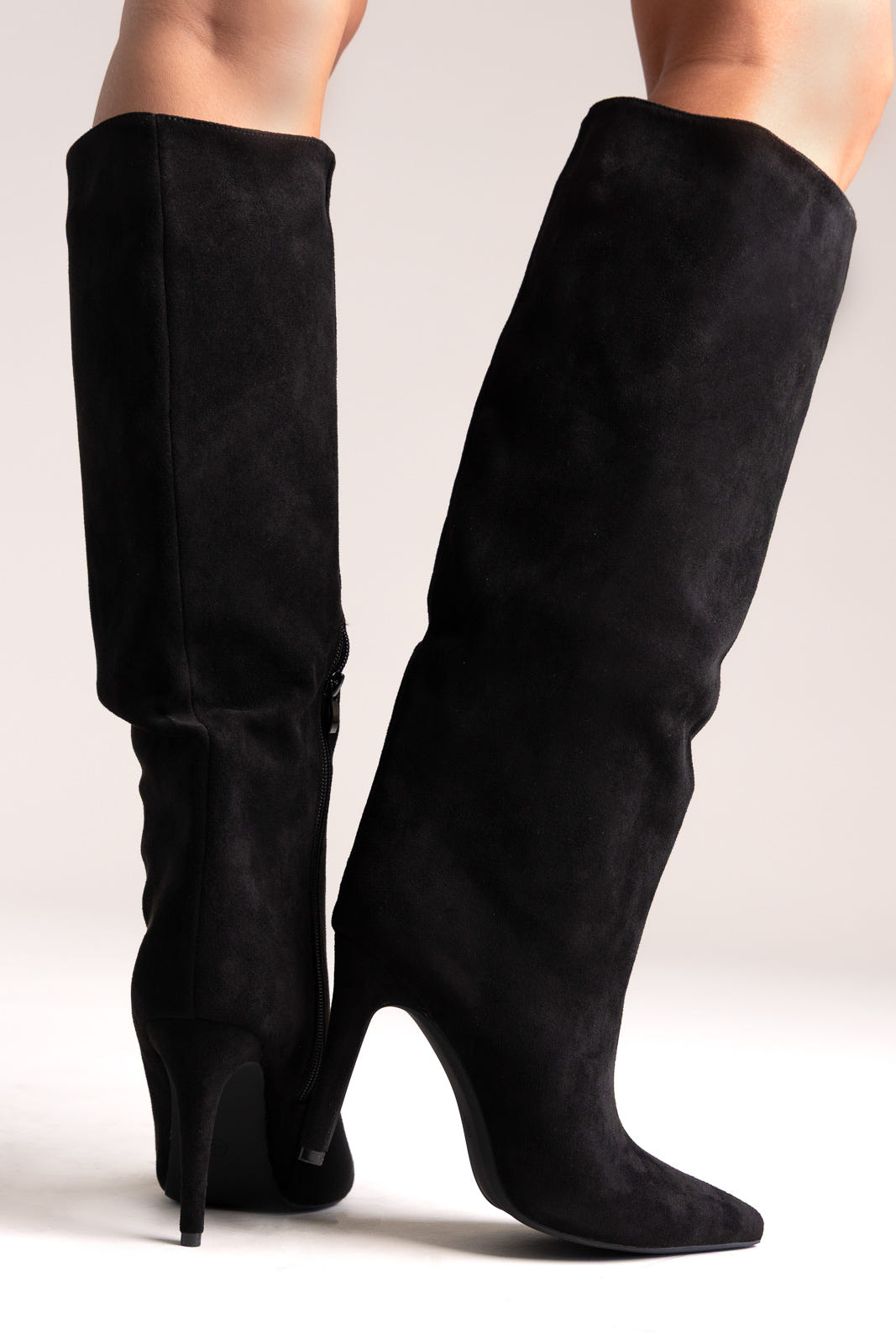 Black faux suede pointed-toe stiletto knee-high boots with slouchy shaft, back view on a model