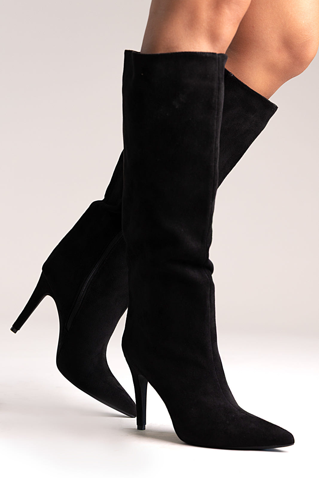 Black faux suede pointed-toe stiletto knee-high boots, angled side view on a model