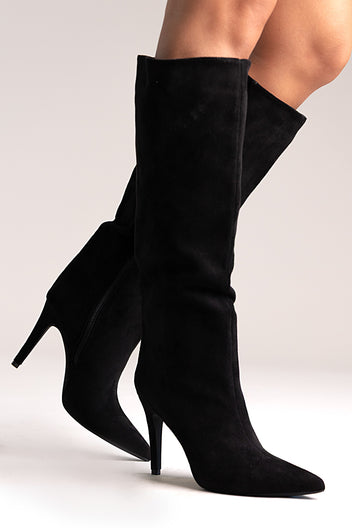 Black faux suede pointed-toe stiletto knee-high boots, angled side view on a model