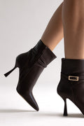 Dark brown leather pointed-toe ankle boots with gold buckle and stiletto heel, angled view on a model
