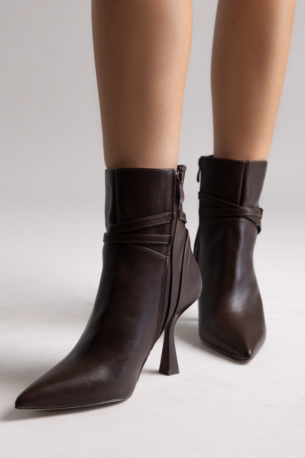 Dark brown leather pointed-toe ankle boots with stiletto heel and side strap, angled view on a model