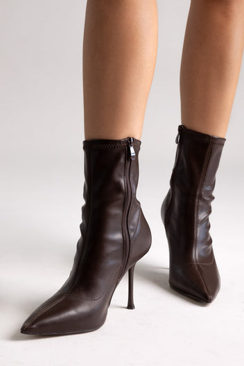 Dark brown leather ankle boots with side zip and stiletto heel, side view on a model in studio light