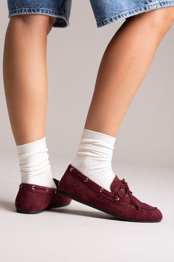 Burgundy faux suede lace-up boat shoes with eyelets, side view on a model in white socks