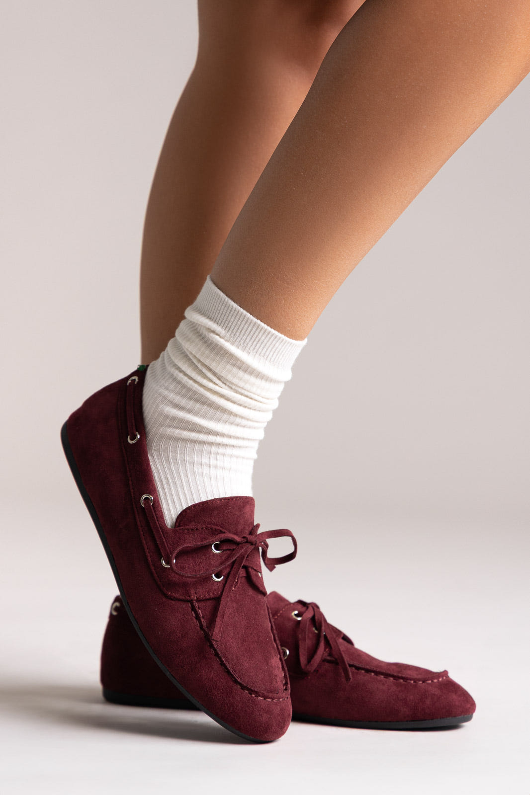 Burgundy faux suede lace-up boat shoes with eyelets, angled view on a model in white socks