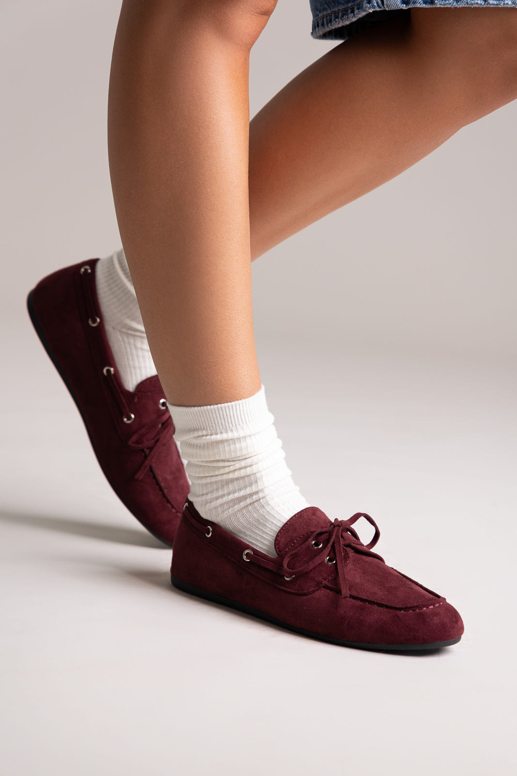 Dark burgundy faux suede stiletto ankle boots with pointed toe, angled view on a model