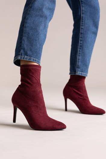 Dark burgundy faux suede stiletto ankle boots with pointed toe, side view on a model in jeans