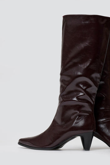 Burgundy crinkled patent leather knee-high boots with pointed toe and cone heel, close-up of the shaft