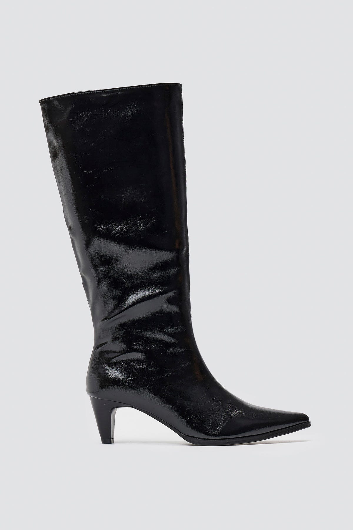 Black crinkled patent leather knee-high boots with pointed toe and cone heel, side view on light grey