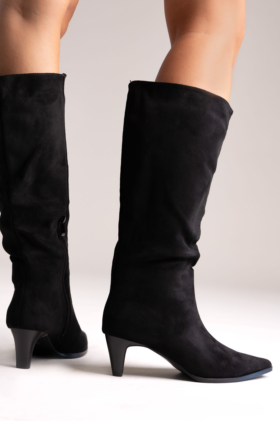 Black faux suede pointed-toe knee-high boots with block-cut heel, back view on a model