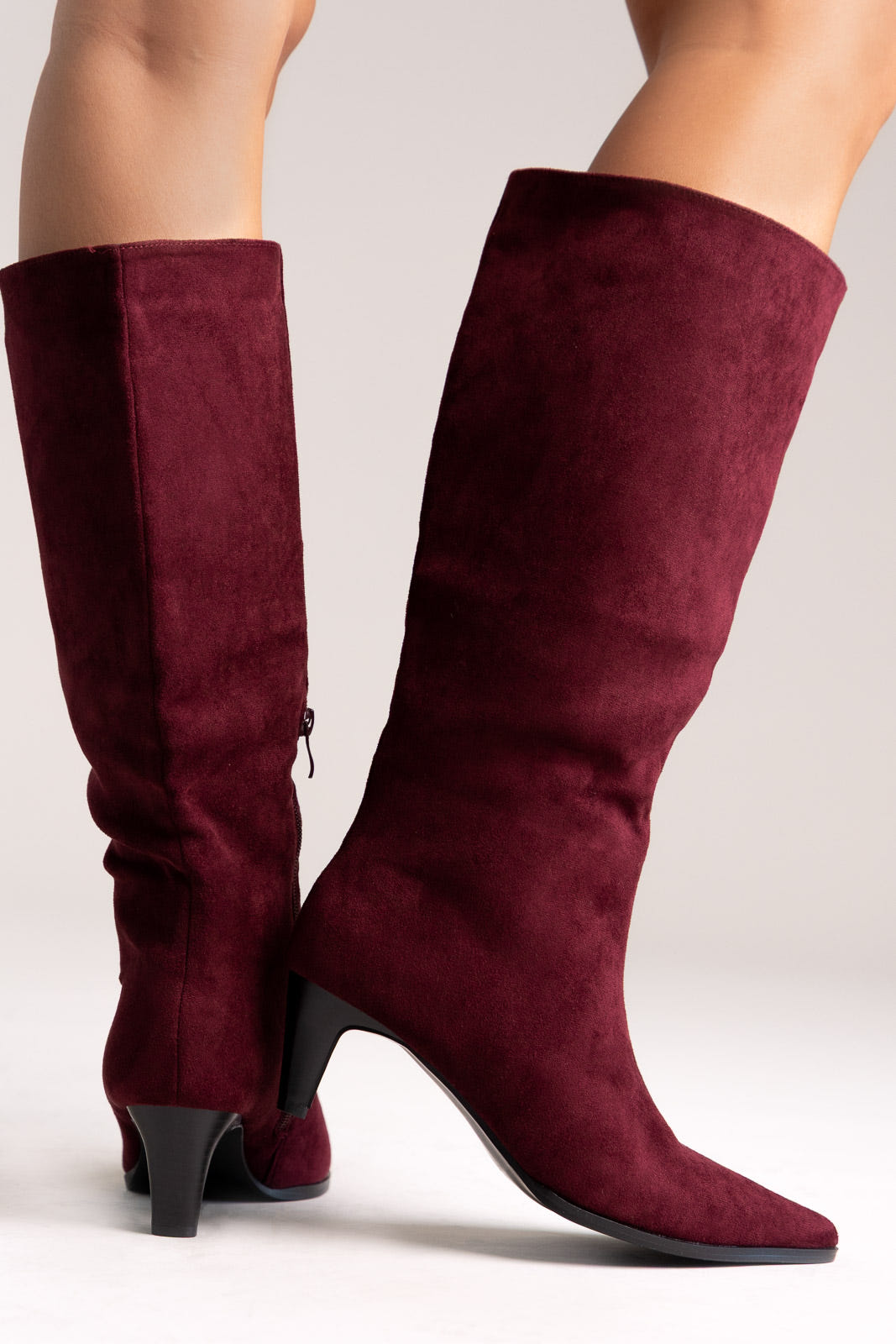 Burgundy faux suede pointed-toe knee-high boots with kitten heel, side view on a model