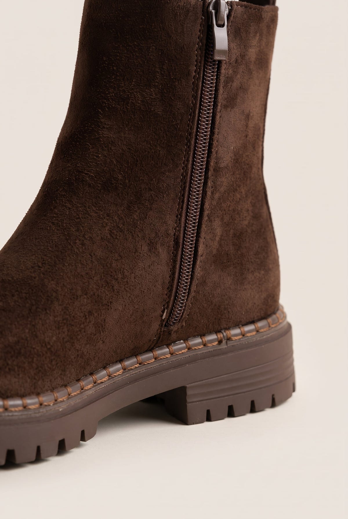 Close-up of mocha brown suede boot shaft and side zipper above a thick lugged rubber sole edge