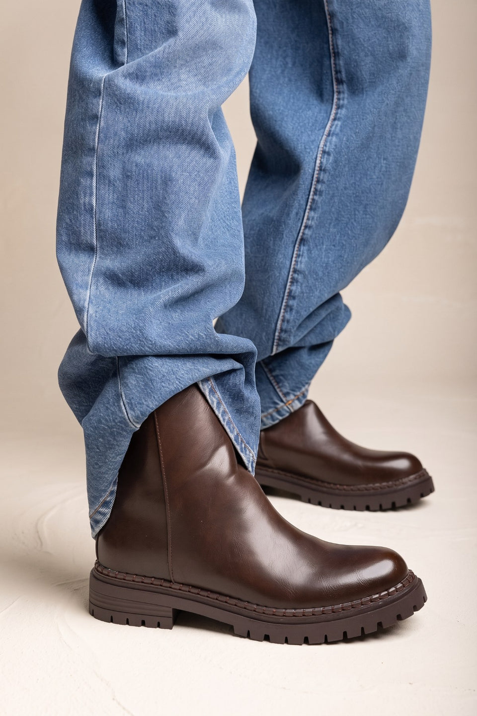 Model wearing wide leg jeans with dark brown matte leather ankle boots featuring chunky lug soles and a rounded toe