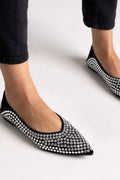 Black suede pointed-toe flats with crystal embellishment, close-up on a model in black jeans
