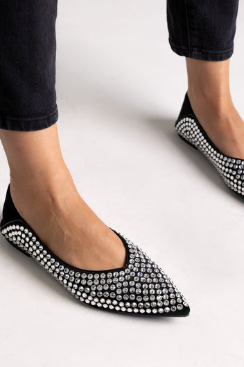 Black suede pointed-toe flats with crystal embellishment, close-up on a model in black jeans