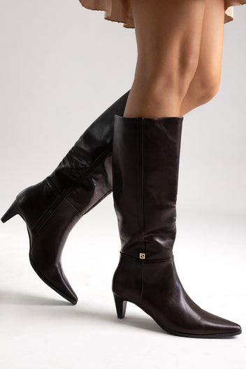 Dark brown leather pointed-toe knee-high boots with buckle detail and kitten heel, angled view on a model