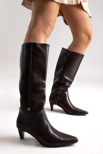 Dark brown leather pointed-toe knee-high boots with kitten heel, side view on a model in studio light