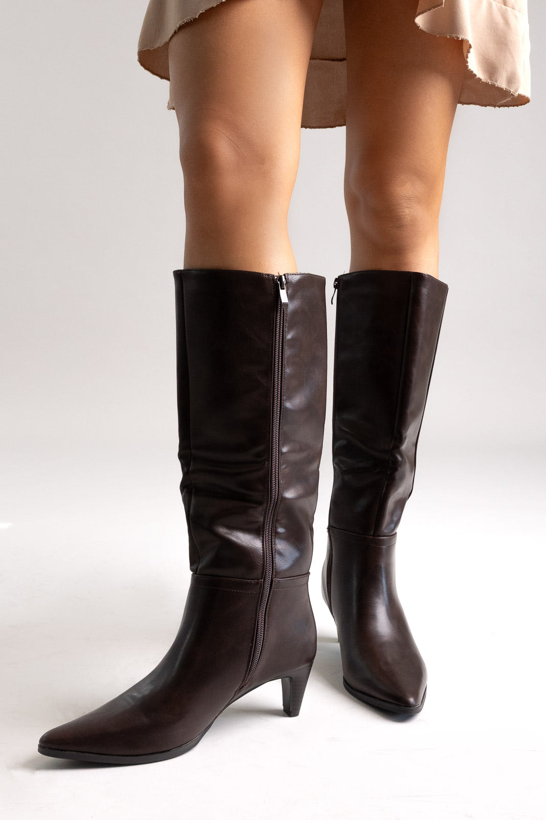 Dark brown leather pointed-toe knee-high boots with side zip and kitten heel, angled view on a model