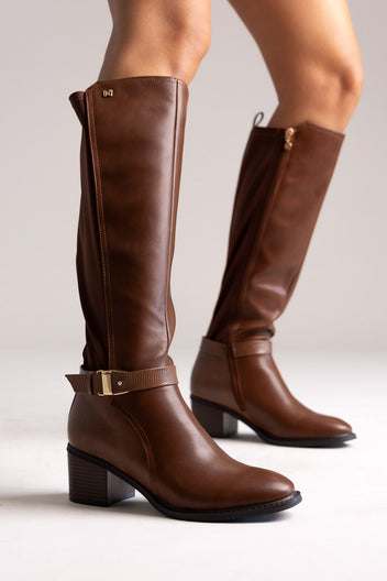 Model legs in tan brown knee-high block heel boots with buckle strap and stretch panel, angled view on a light background