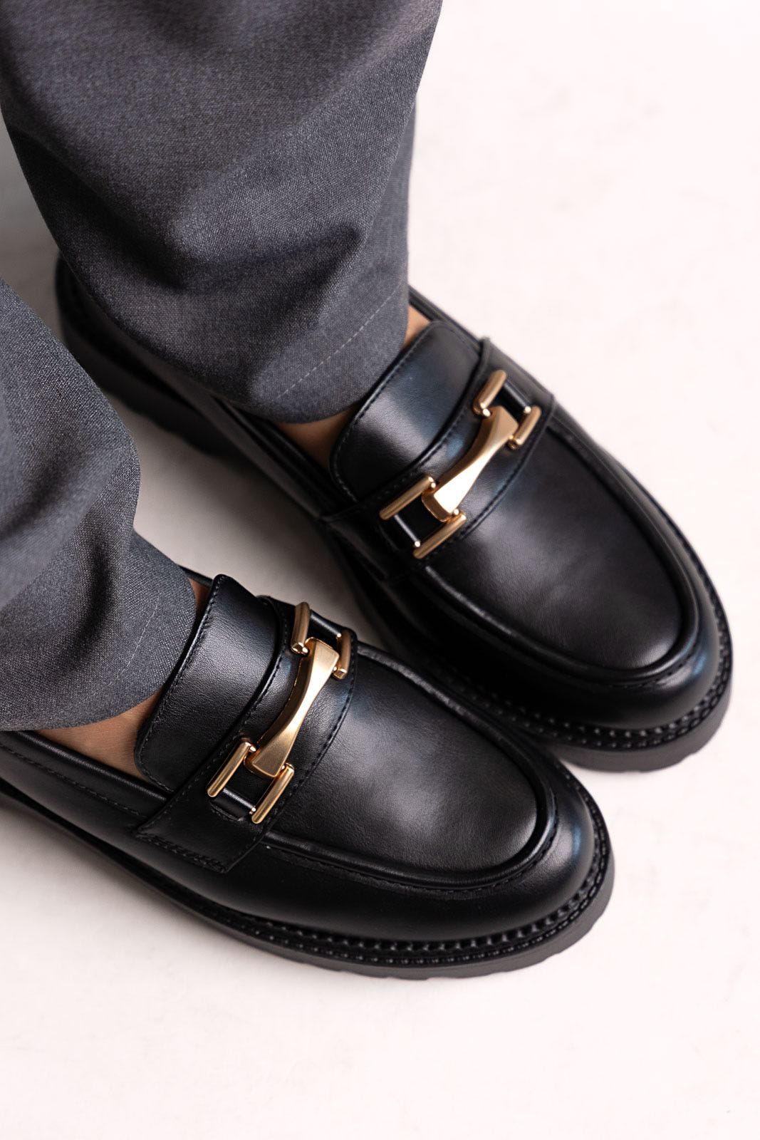 Black leather chunky loafers with gold-tone bit and lug sole, close-up on a model