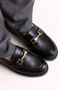 Black leather chunky loafers with gold-tone bit and lug sole, close-up on a model
