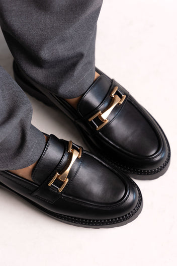 Black leather chunky loafers with gold-tone bit and lug sole, close-up on a model