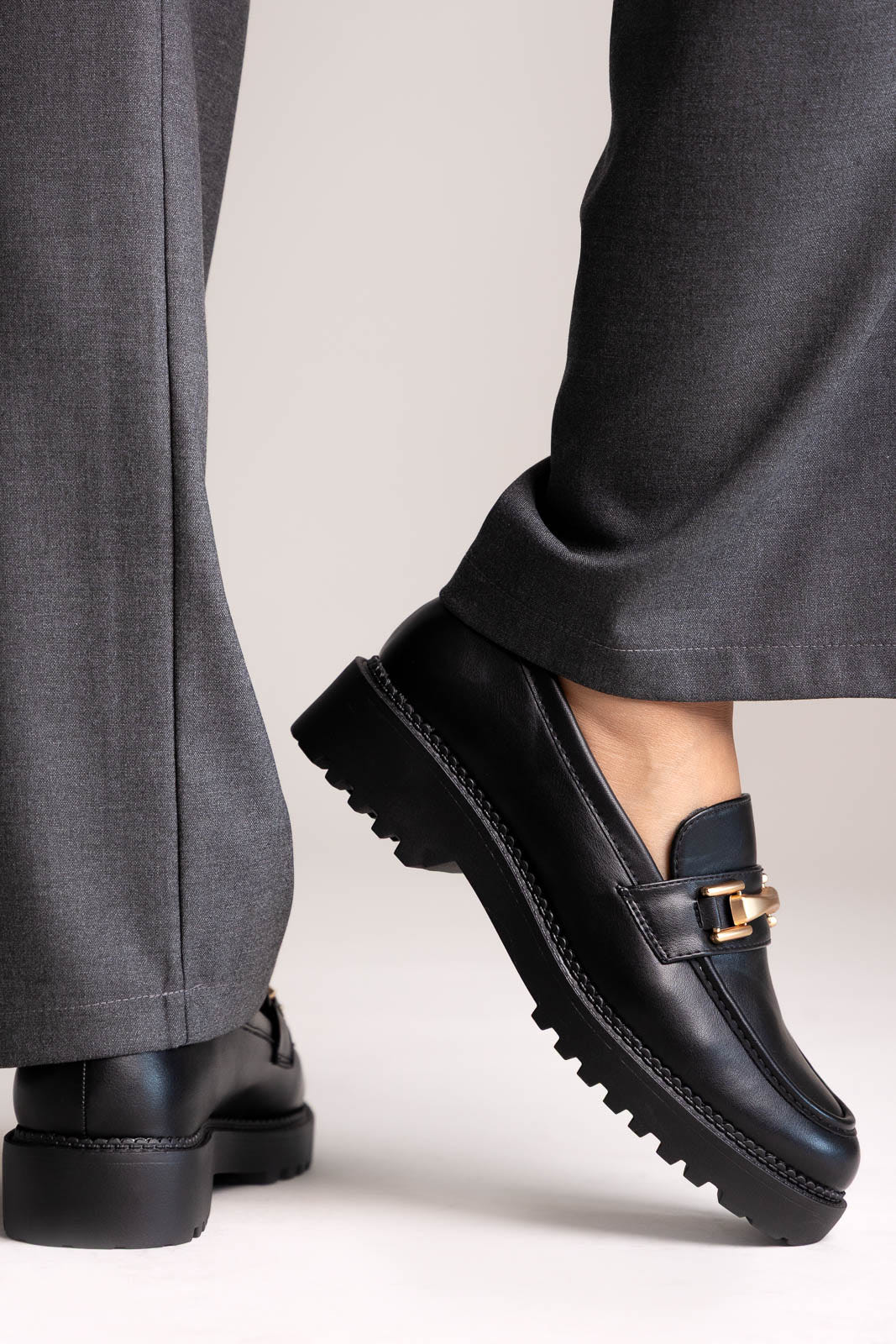 Black leather chunky loafers with gold-tone bit and lug sole, side view on a model