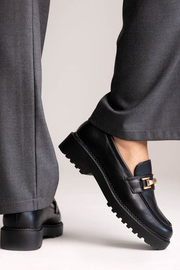 Black leather chunky loafers with gold-tone bit and lug sole, side view on a model