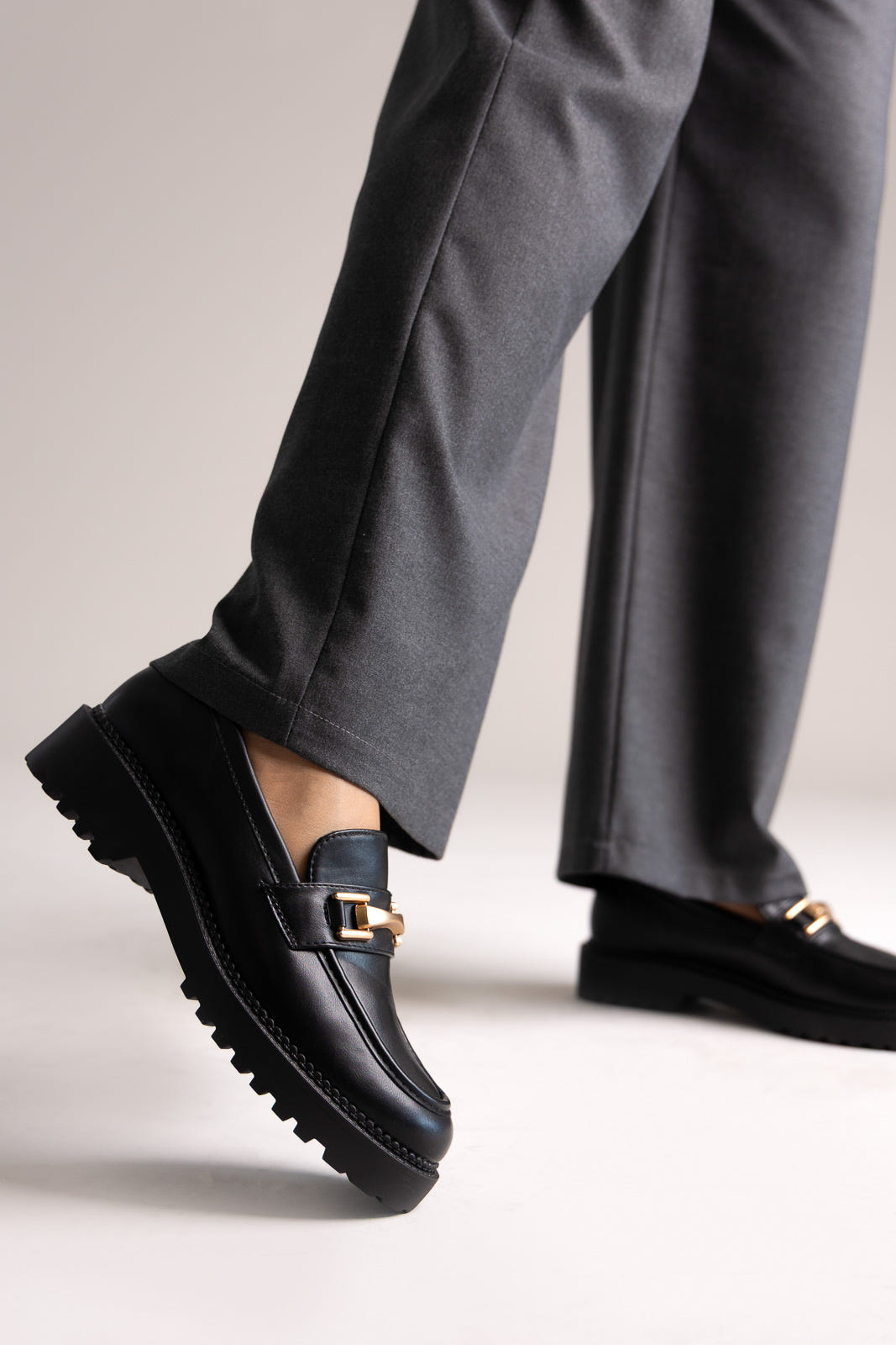 Black leather chunky loafers with gold-tone bit and lug sole, angled view on a model