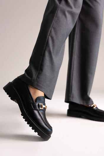 Black leather chunky loafers with gold-tone bit and lug sole, angled view on a model