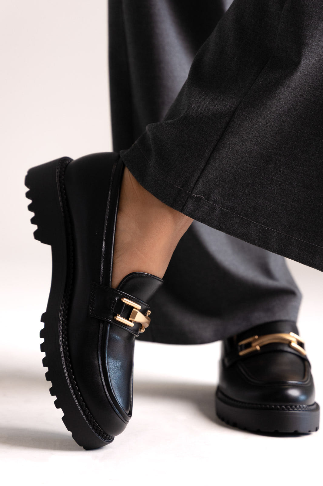 Black leather chunky loafers with gold-tone bit and lug sole, side view on a model