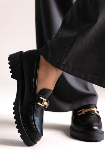 Black leather chunky loafers with gold-tone bit and lug sole, side view on a model