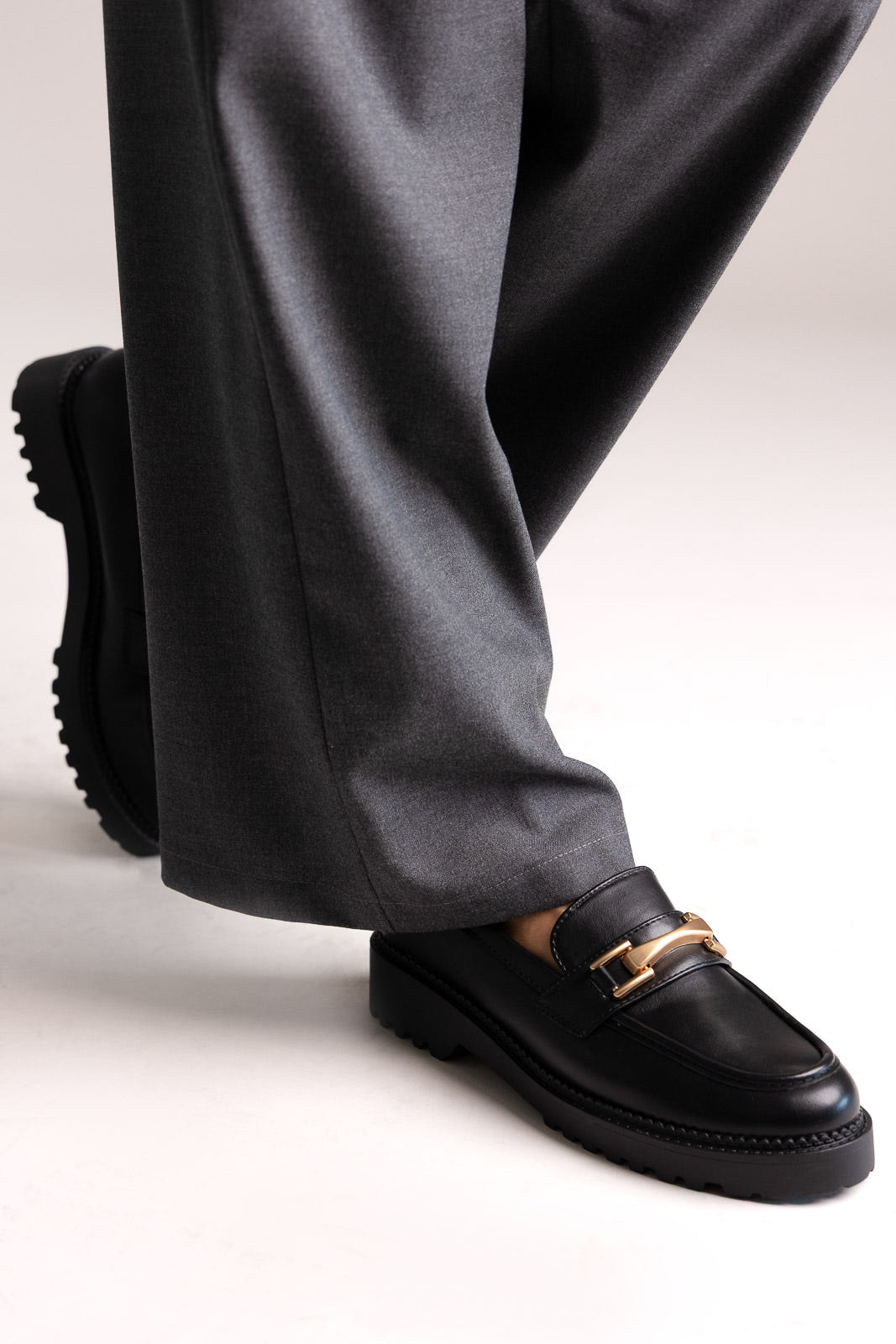 Black leather chunky loafers with gold-tone bit and lug sole, angled view on a model