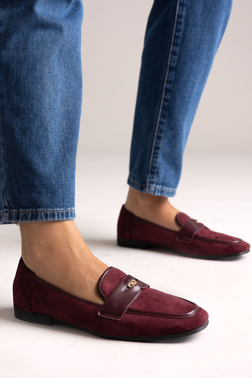 Burgundy suede penny loafers with leather trim and gold-tone bit, side view on a model