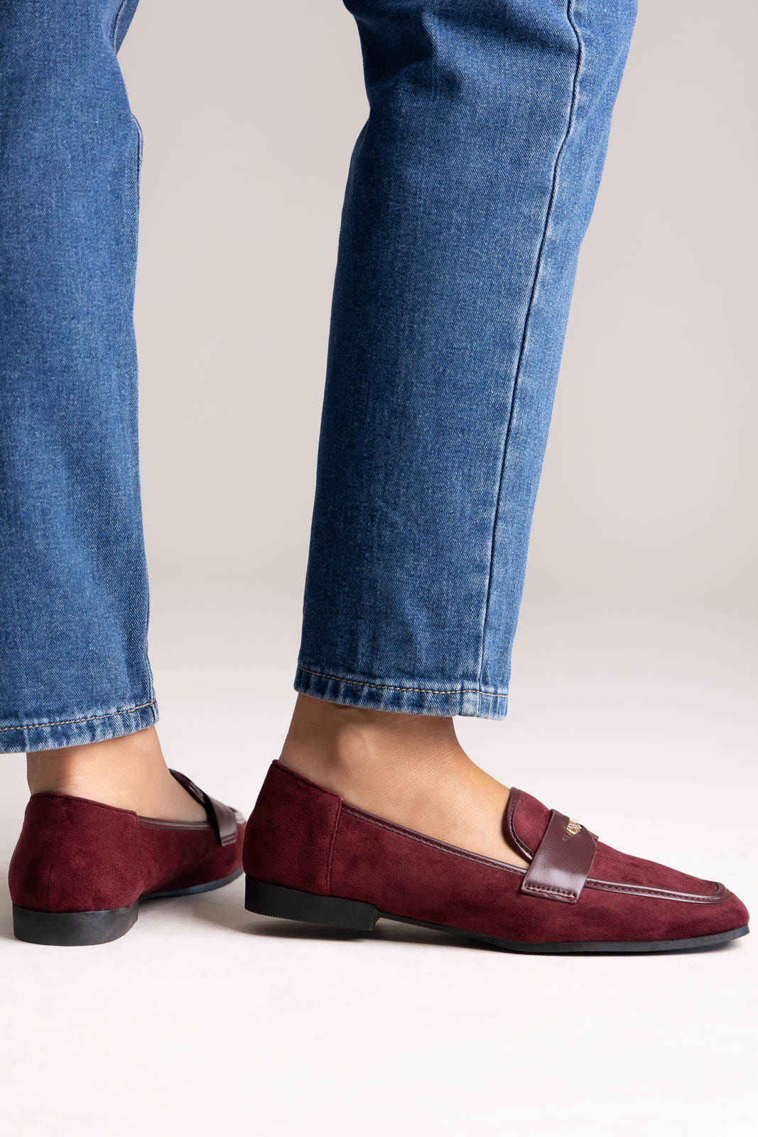 Burgundy suede penny loafers with leather trim and gold-tone bit, angled view on a model in jeans