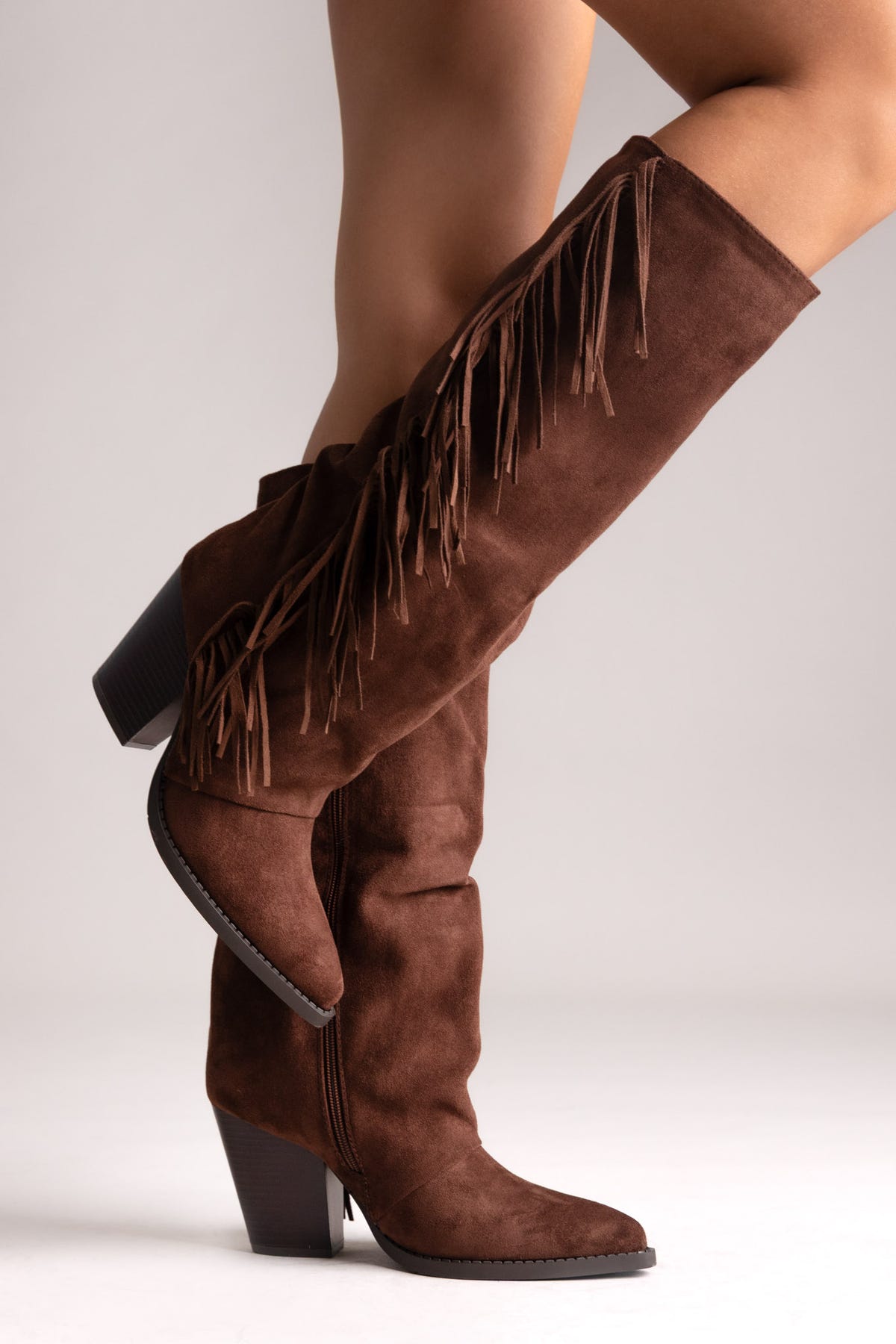 Brown suede knee-high western boots with fringe trim and block heel, side view on a neutral background