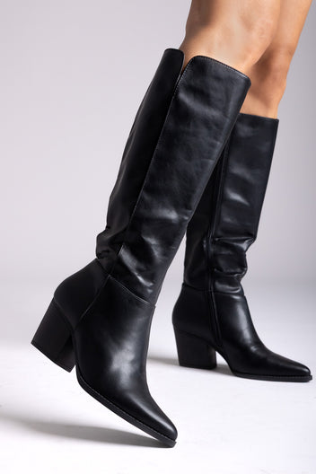 Black leather knee-high boots with pointed toe and block heel, angled view on a model in studio light