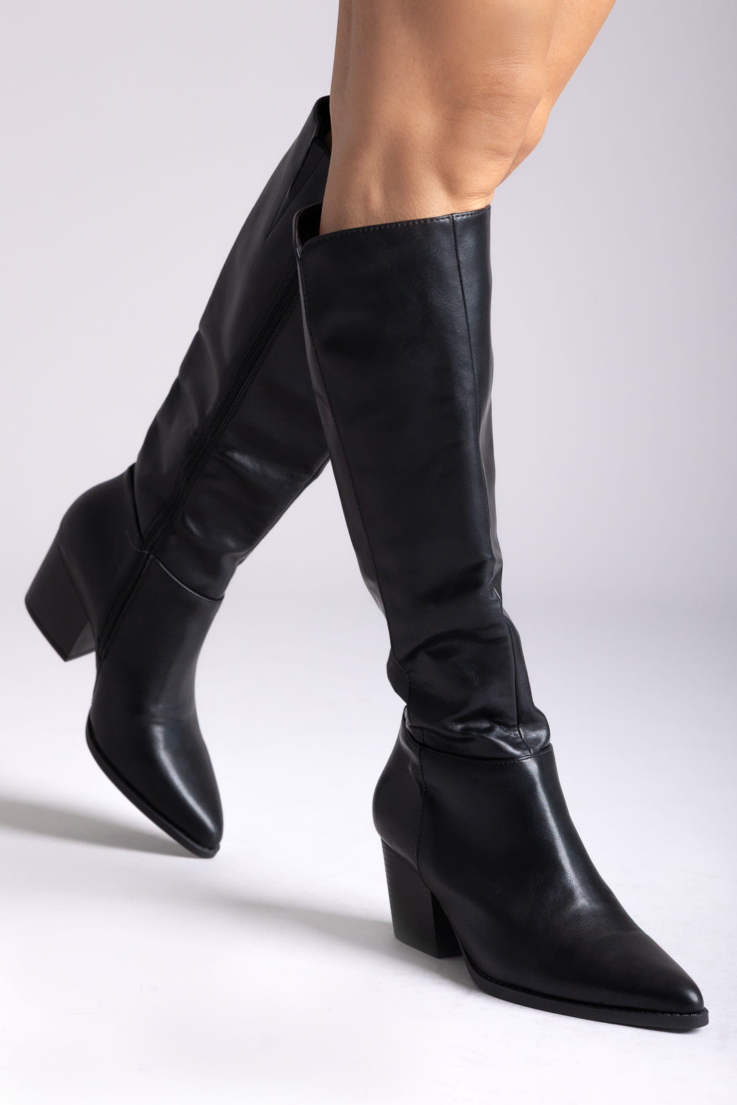 Black leather knee-high boots with pointed toe and block heel, side view on a model in studio light
