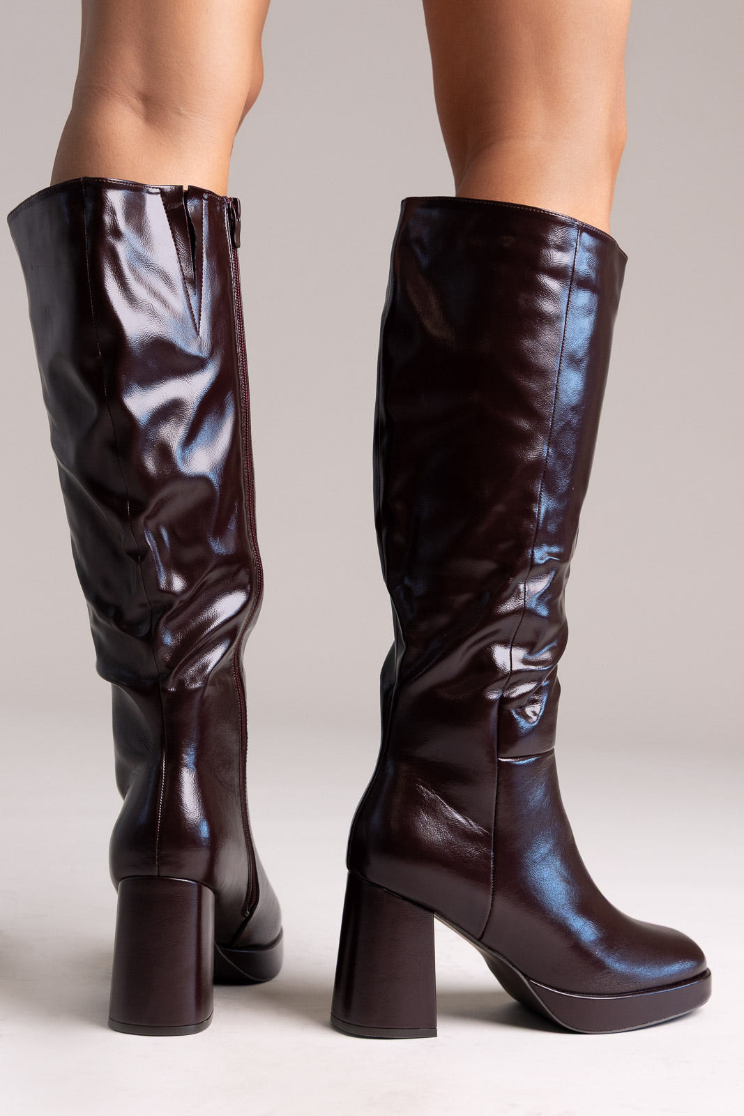 Dark burgundy glossy faux leather knee-high boots with platform and block heel, back view on a model