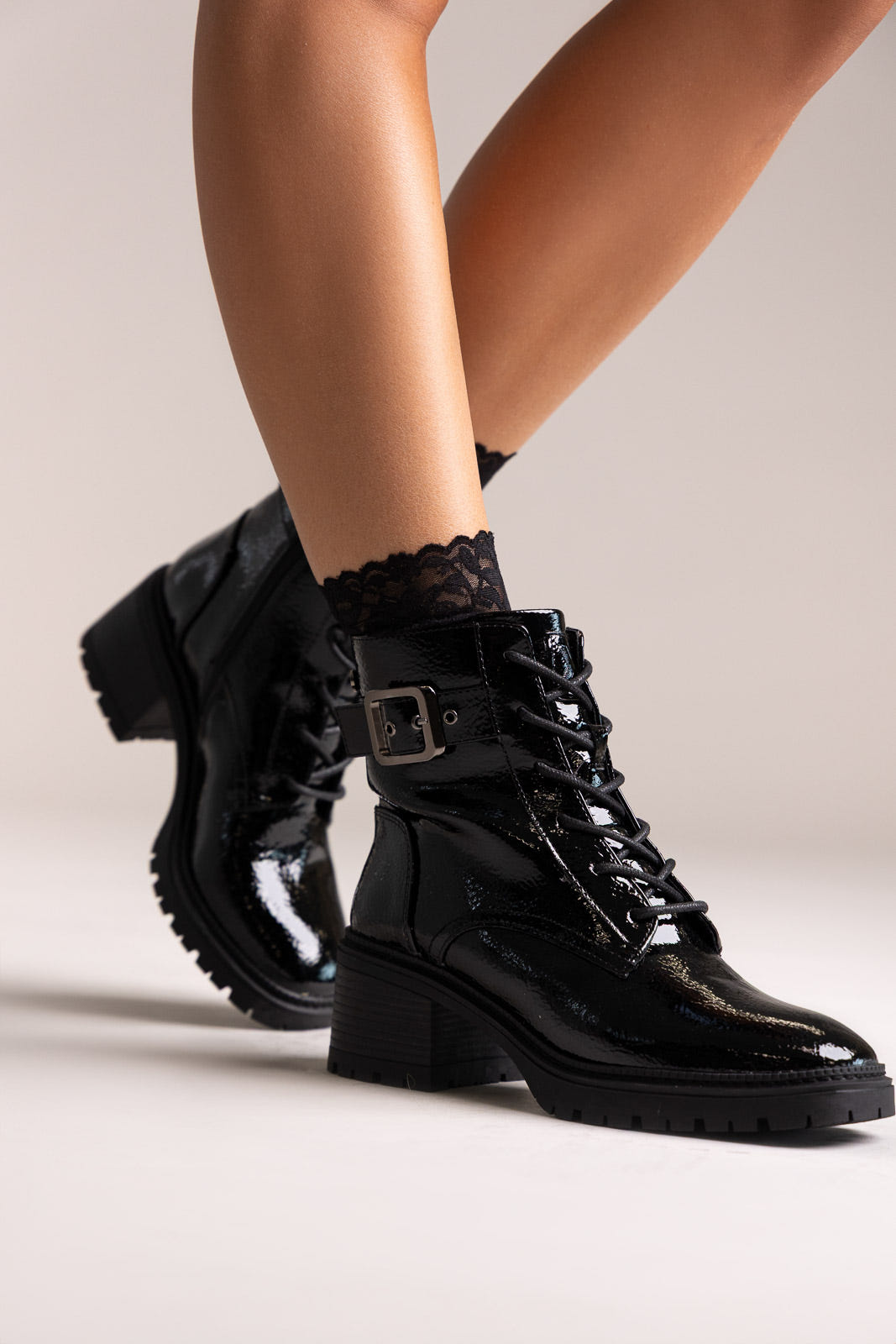 Black crinkled patent lace-up combat boots with buckle strap and block heel, angled view on a model