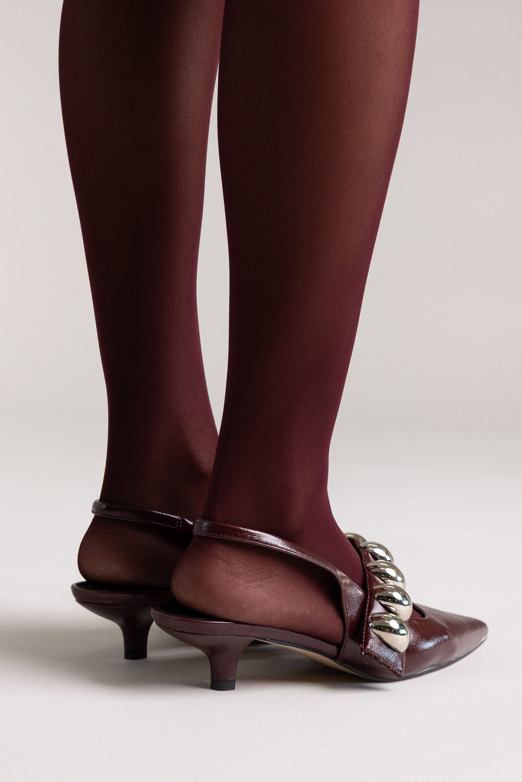 Burgundy leather pointed-toe slingback kitten heels with silver ball-chain strap, rear view on a model