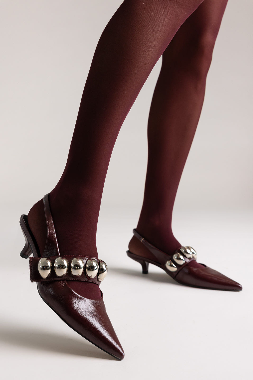 Burgundy leather pointed-toe slingback kitten heels with silver ball-chain strap, front view on a model