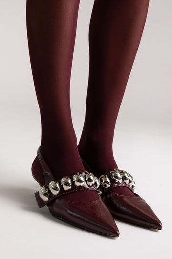 Burgundy leather pointed-toe slingback kitten heels with silver ball-chain strap, front view on a model in tights