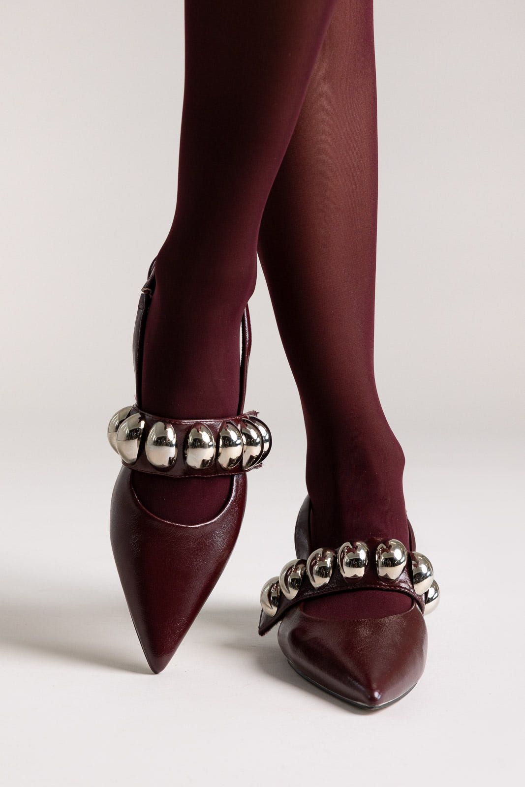 Burgundy leather pointed-toe slingback kitten heels with silver ball-chain strap, angled view on a model
